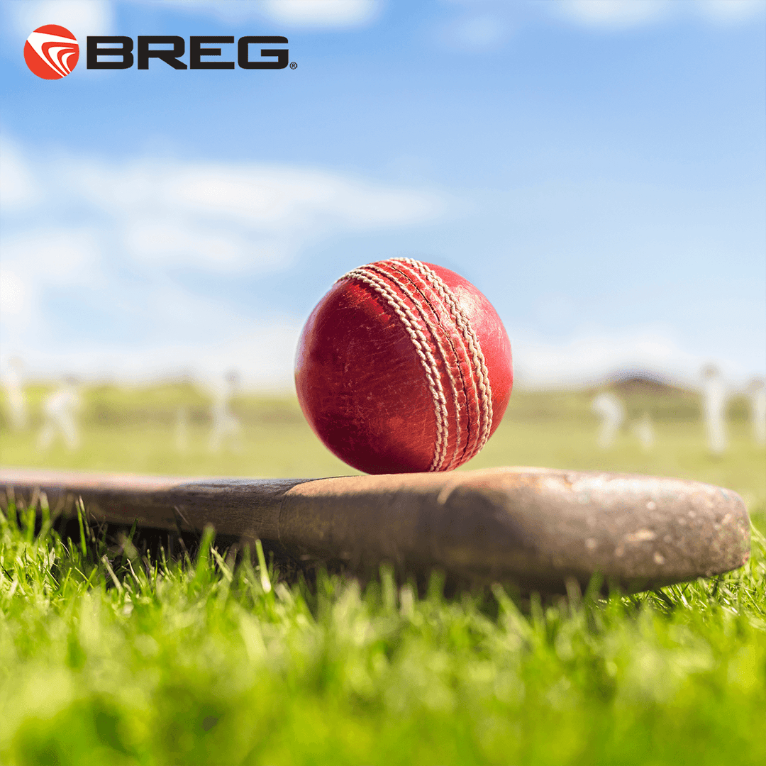 Close-up of a red cricket ball on a bat with players on a sunny cricket field and Breg logo
