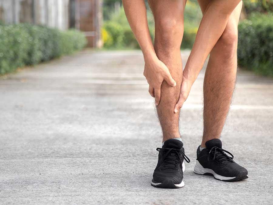 Person in black sneakers holding lower leg, indicating shin splint pain outdoors on pavement